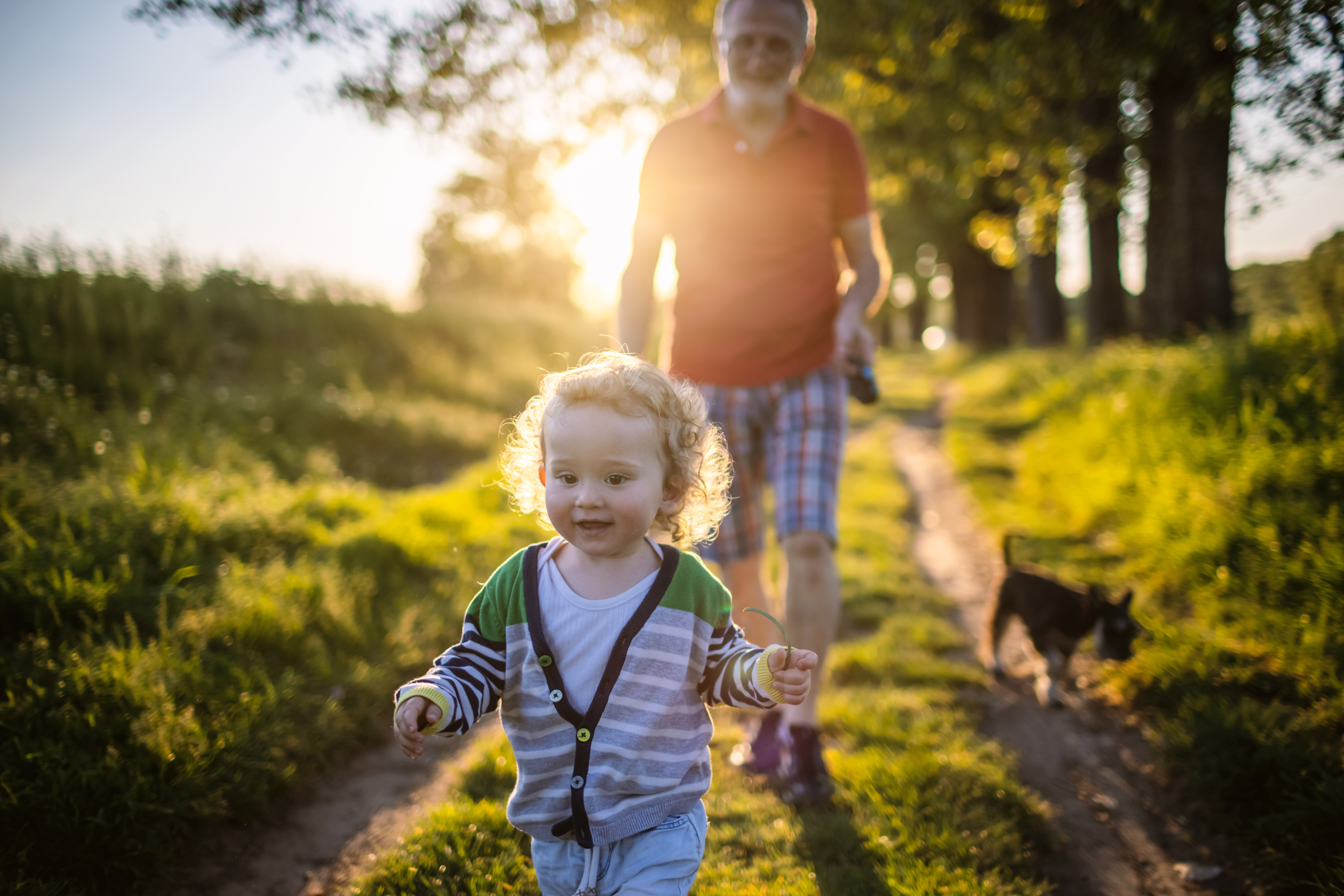 Photo of a little boy and his grandfather walking outdoors with their dog, enjoying in nature.